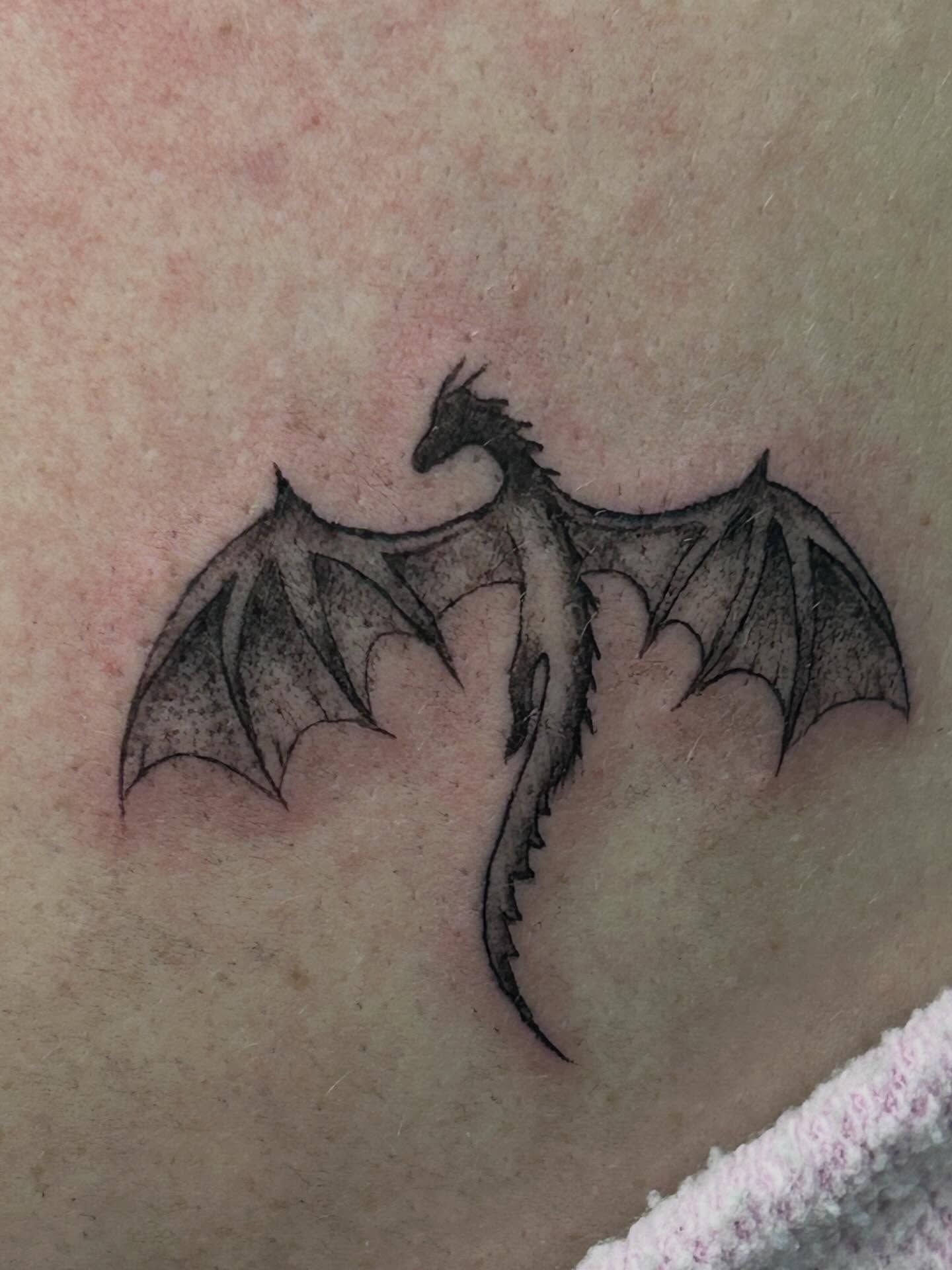 Close-up of a dragon with outspread bat-like wings and a spiked tail, softly shaded in black and grey