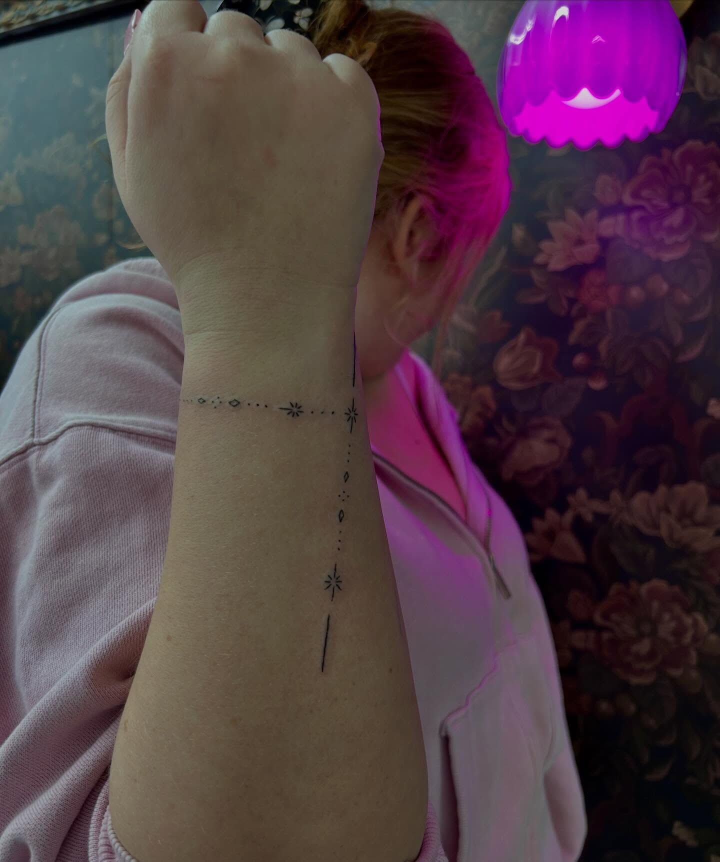 A delicate wrist bracelet of dots and diamonds with a star, and a dotted line running down the forearm