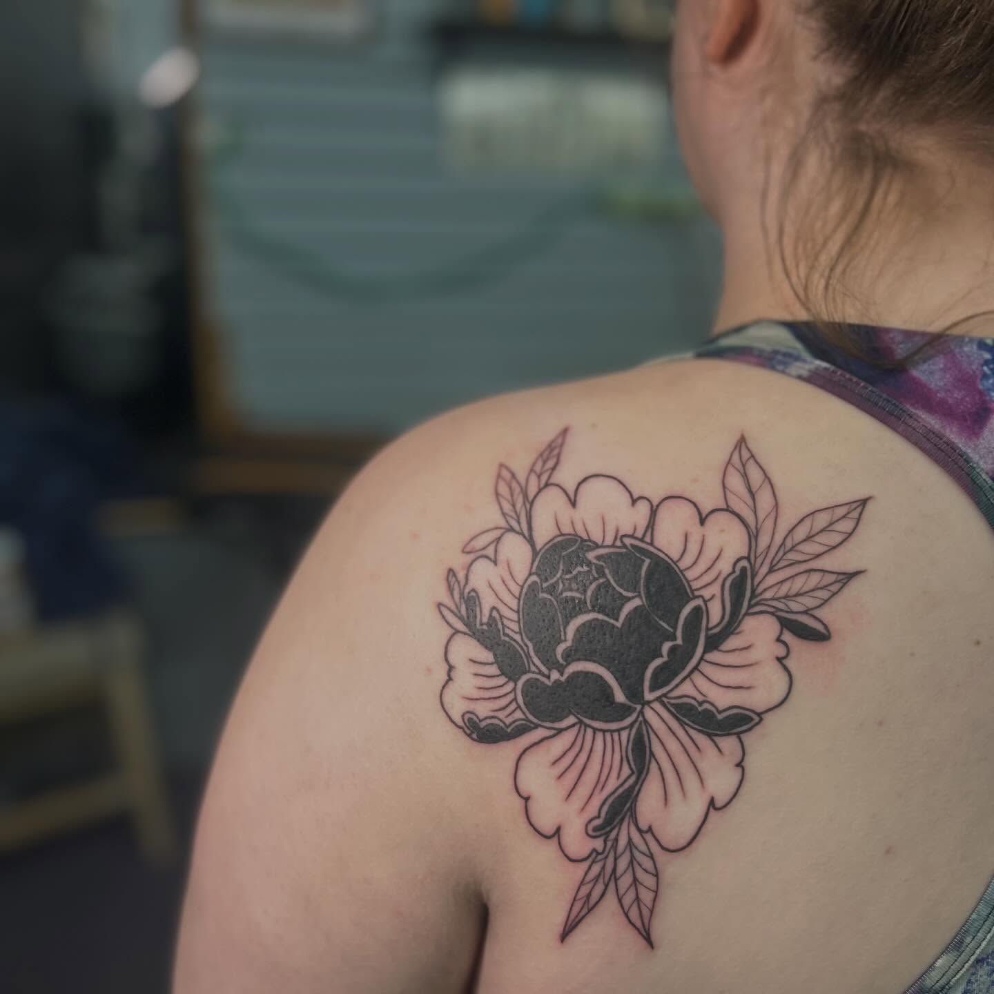 A bold peony in black and grey on a shoulder blade