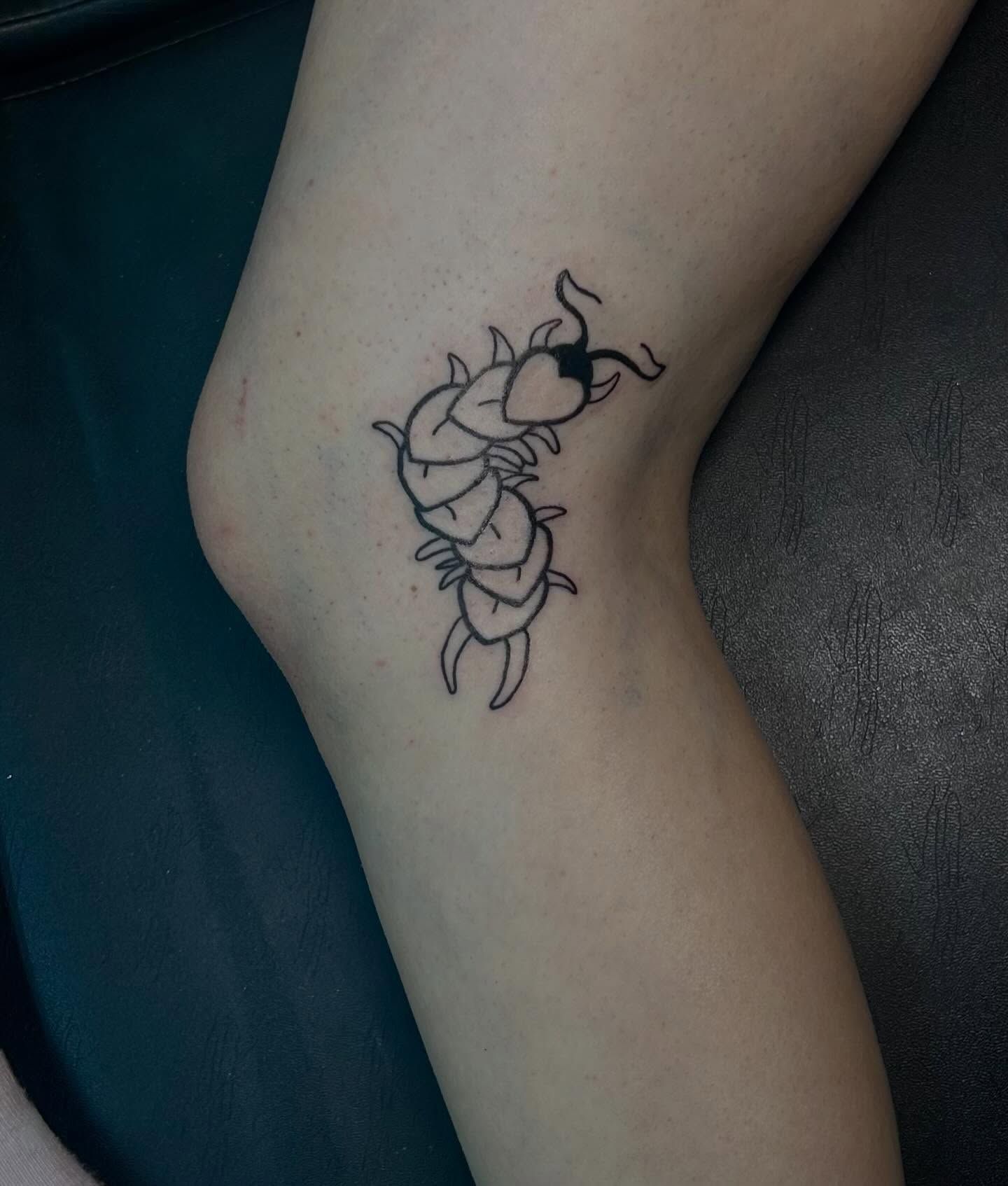 A centipede with heart-shaped body segments and curling antennae, outlined on the back of an ankle